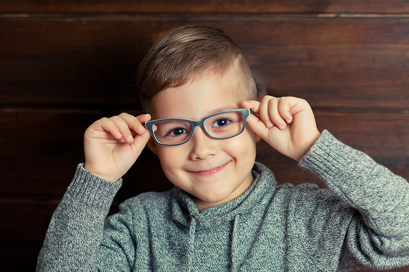 young boy smiling holding glasses near face